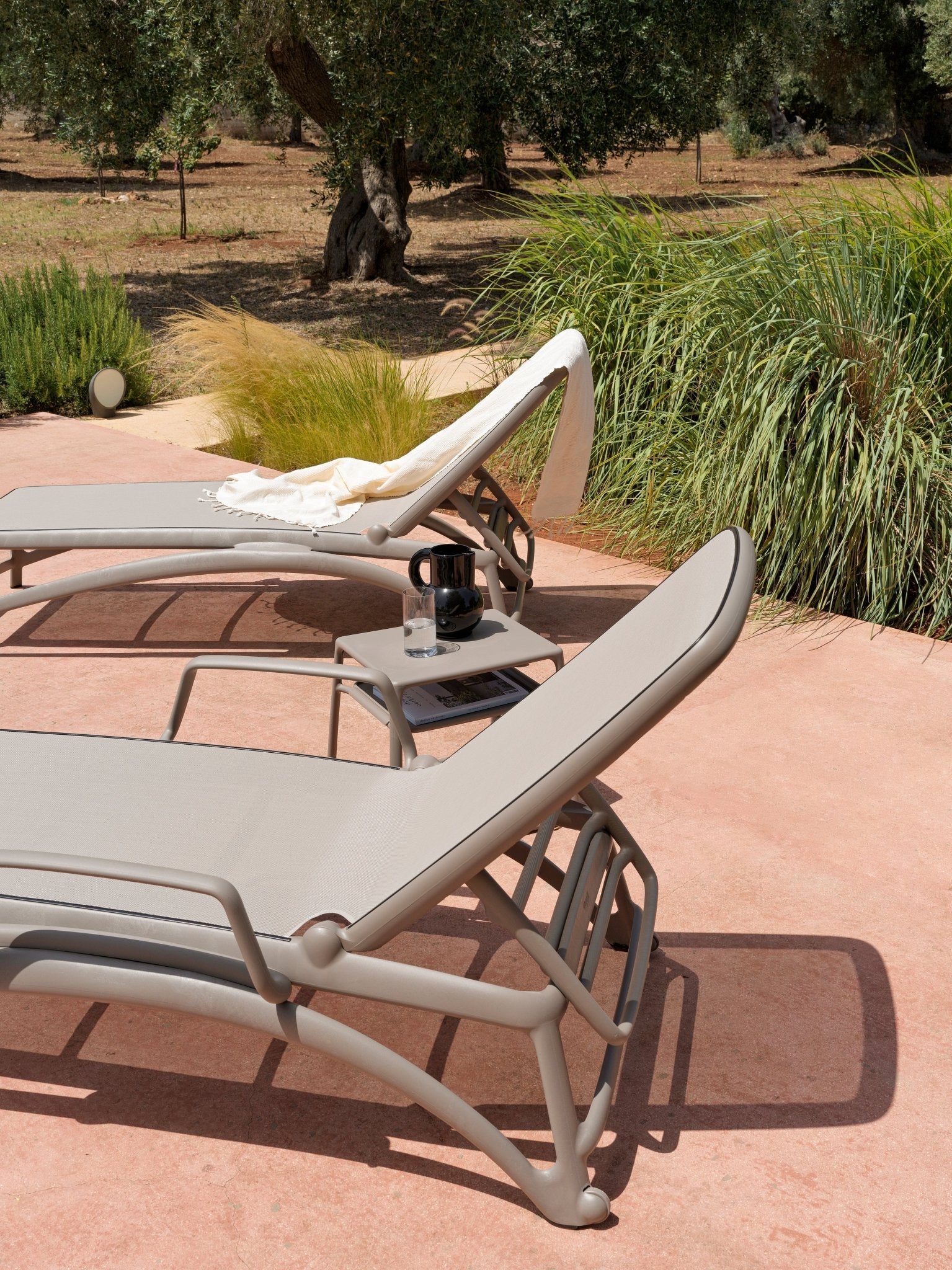 Reposeras Atlántico con Apoyabrazos Nardi Italia color Tortora — ambiente de terraza junto a olivos y pastos ornamentales, con mesa lateral — bCasual
